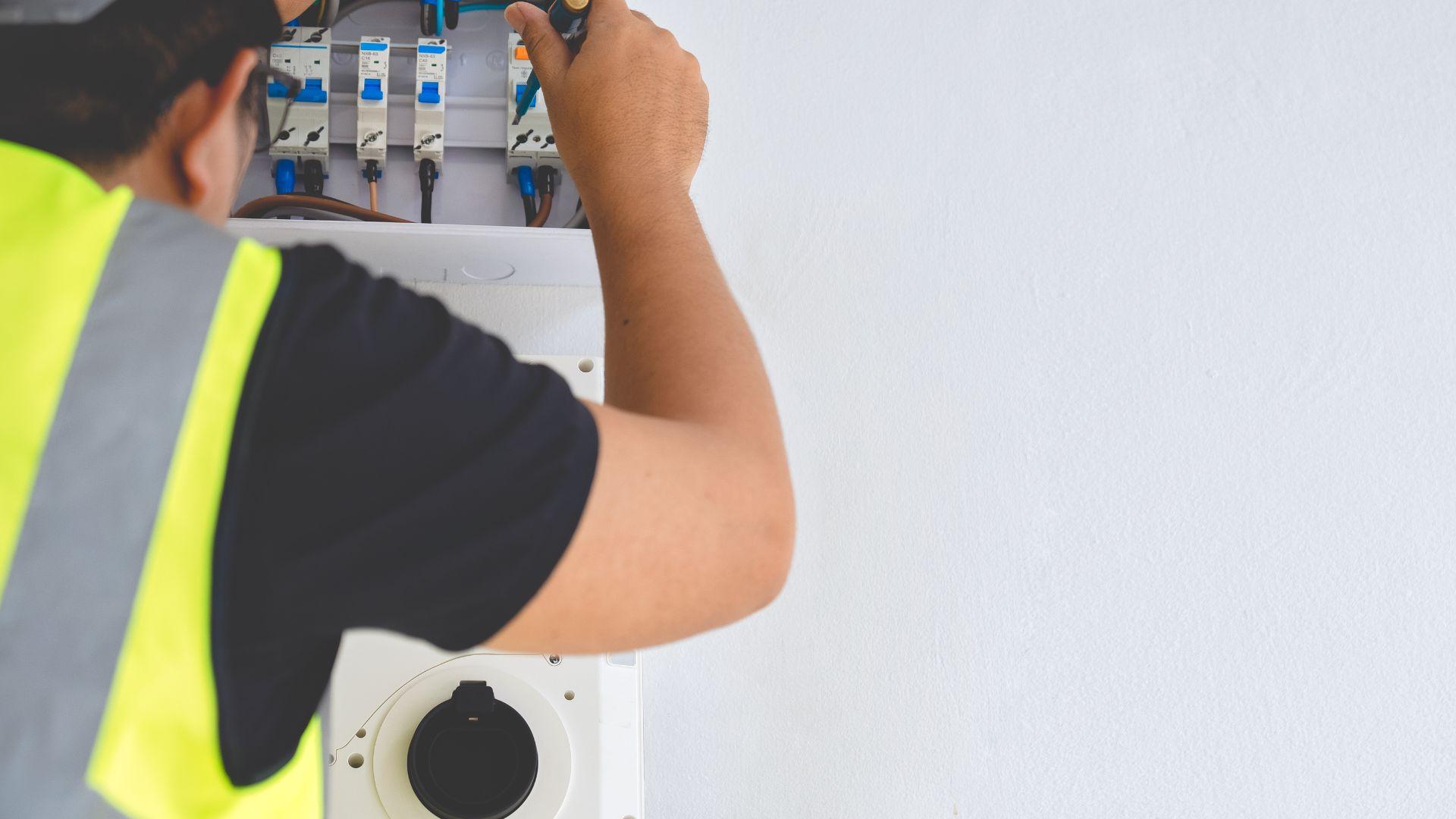 Electrician in safety vest installing electrical panel